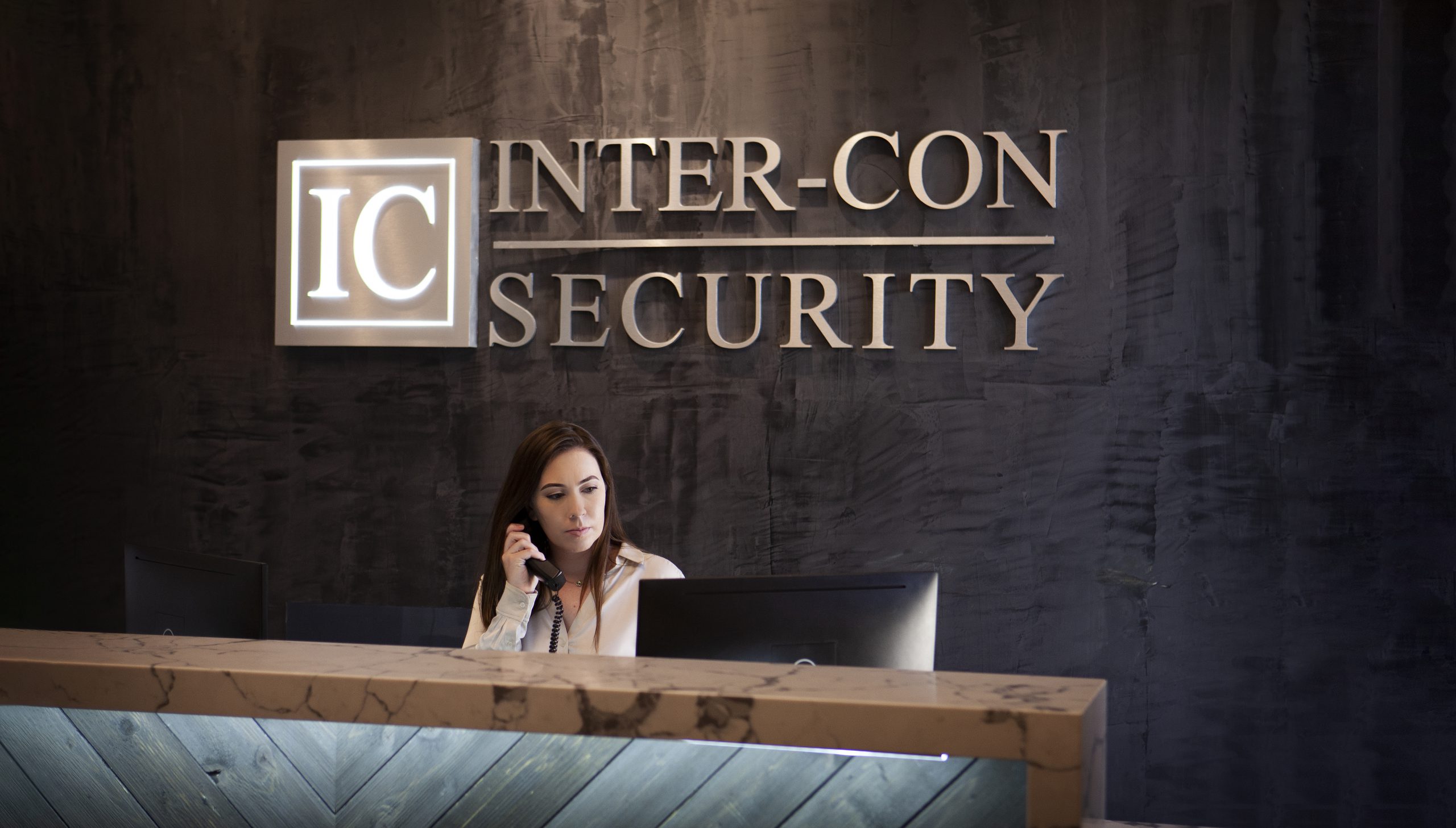 Concierge receptionist with phone sitting behind desk at inter-con security building